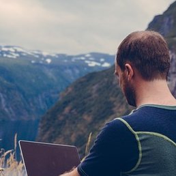 Digital nomad working on cryptocurrency project on laptop with mountains in background.